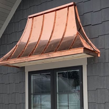 Curved copper window canopy on a shingle-clad home